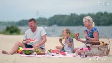 暑假快乐的一家人坐在沙滩上五颜六色的毯子上，野餐的一家人带着孩子吃西瓜
